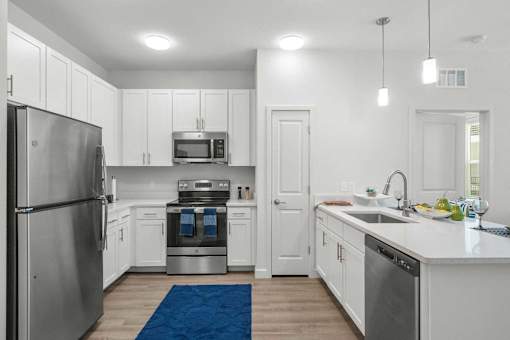 Luxury Apartments In St. Petersburg, FL With In-Unit Washer And Dryer - Gallery 3100 - A Modern Kitchen With An Island, Stainless Steel Ge Appliances, And A Vibrant Blue Rug On Wood-Style Flooring.