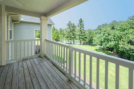 A wooden porch with a view of a green lawn and trees.