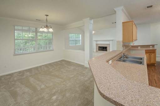 A large, empty living room with a fireplace and a kitchen area in the background.
