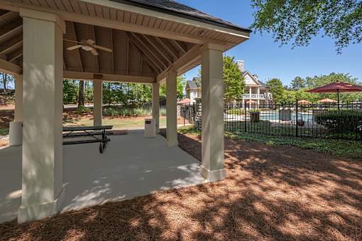 A covered patio area with a bench and a pool in the background.