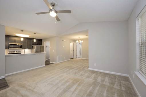 A spacious living room with a ceiling fan and lighting fixtures.