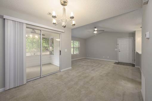 A room with a chandelier, sliding glass doors, and a carpeted floor.