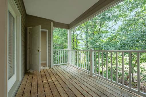 A wooden deck with a white railing and a door leading to a lush green forest.
