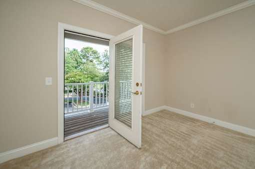 A room with a white door and a window showing a view of trees and a parking lot.