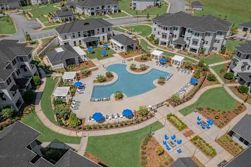 A large swimming pool surrounded by blue lounge chairs and umbrellas is the centerpiece of a resort-style community.