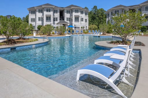 a large pool with white and blue chairs in front of an apartment building