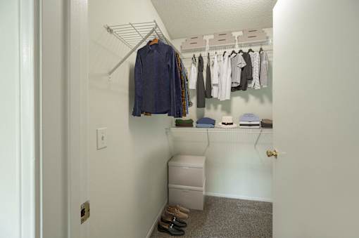 A white closet with clothes hanging and a white trash can.