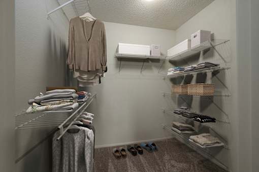 A room with a hanger on the wall and clothes on the shelves.