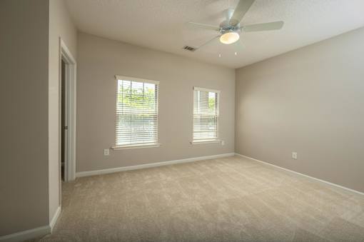 A room with a ceiling fan and two windows.