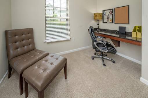 A brown leather chair and ottoman are in a room with a desk and a window.