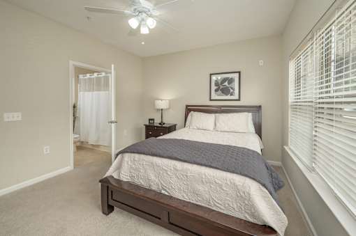 A bedroom with a bed, nightstand, and window with blinds.