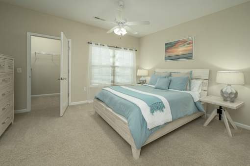 A bedroom with a bed, a dresser, a ceiling fan, and a painting on the wall.