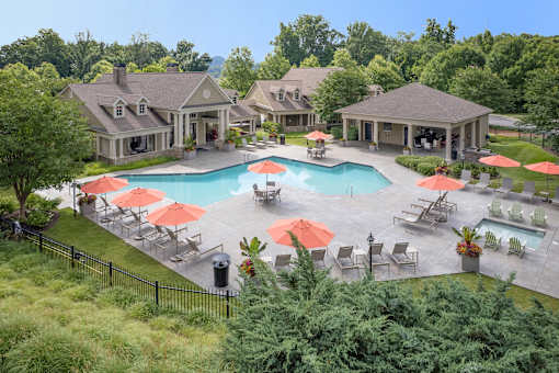 A large outdoor swimming pool surrounded by red umbrellas and lounge chairs.