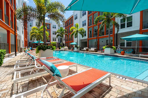 A pool with sun loungers and umbrellas in front of a building.
