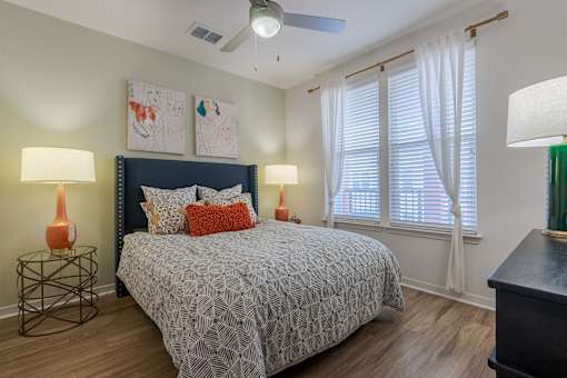 2-Bedroom Apartments in Tampa, FL - Havana Square - Bedroom with Vinyl Plank Flooring, Large Bed, Nightstands with Lamps, Wall Art, Ceiling Fan, Dresser with Lamp, and Large Window with Coverings.