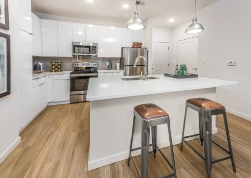 1-Bedroom Apartments in Tampa, FL - Havana Square - Kitchen with Vinyl Plank Flooring, Granite Countertops, Designer Cabinetry, Tile Backsplash, Stainless Steel Appliances, Kitchen Island with Bar-Stool Seating, and Pendant Lights.