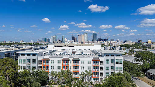 A large white building with orange accents is in the foreground with a city skyline in the background.