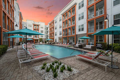 A pool surrounded by lounge chairs and umbrellas in a courtyard.