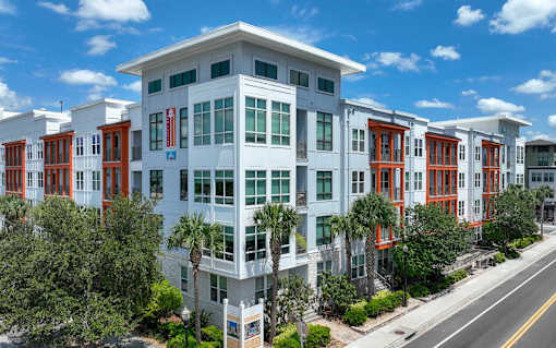 A white building with red doors and windows is surrounded by trees.