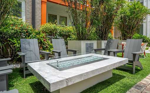 A modern outdoor seating area with a glass table and grey chairs.