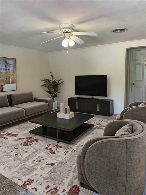 A living room with a grey sofa, a black coffee table, a flat screen TV and a ceiling fan.