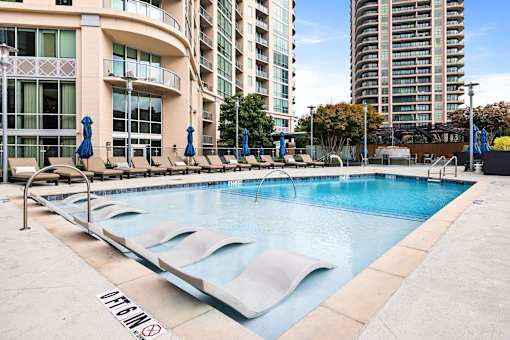 Luxury Apartments in Buckhead, GA, With In-Unit Washer and Dryer - The Huntley - Resort-Style Swimming Pool With In-Water Lounge Chairs, Sundeck Seating, Blue Umbrellas, and High-Rise Views.