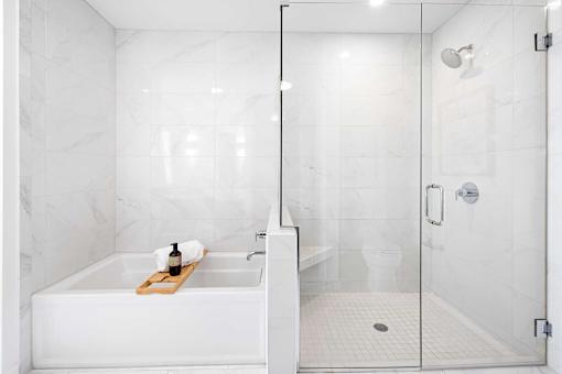 A white bathroom with a marble wall and a glass shower door.