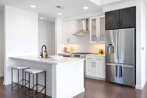 Luxury Apartments Near Lenox Square Mall In Buckhead, GA - The Huntley - Kitchen With Luxurious Tuscany and Rocksalt Quartz Counter-Tops, Stainless-Steel Appliances, Genuine Hardwood Floors, Kitchen Island, And White Cabinets.