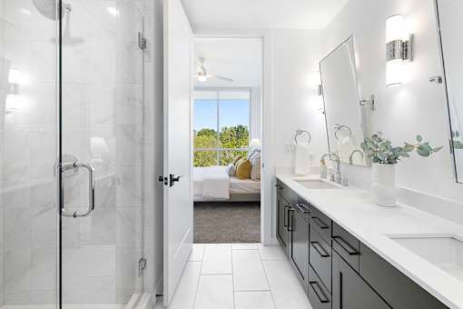 A bathroom with a walk-in shower, a vanity with a mirror, and a view of a backyard through the door.