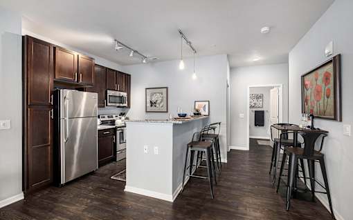 A kitchen with a refrigerator, microwave, oven, and bar stools.