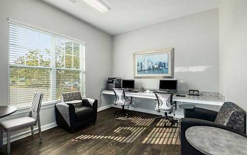 A room with a desk, chairs, and a painting on the wall.