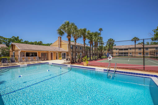 a swimming pool with a tennis court and a building with palm trees