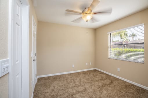 an empty bedroom with a ceiling fan and a window