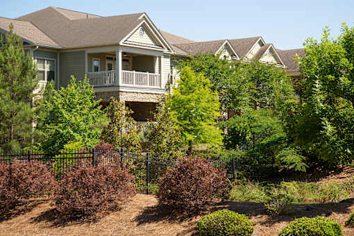 A house with a brown roof and a balcony surrounded by green trees and bushes.