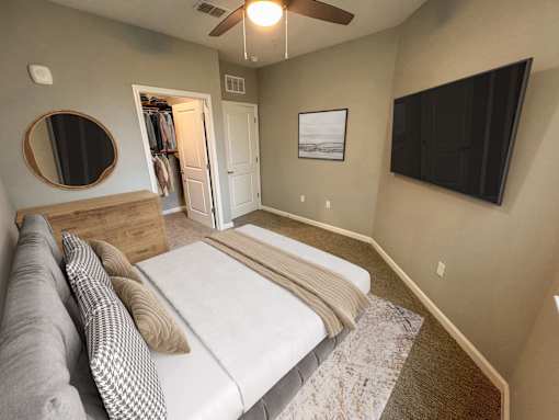 A bedroom with a bed, a couch, a mirror, and a ceiling fan.