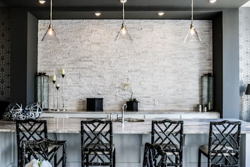 A kitchen with a white brick wall and black chairs.