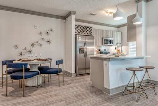 Two-Bedroom Luxury Apartments In Sarasota, FL - Botanic Waterside - Kitchen With Wood-Finish Flooring, Stainless Steel Appliances, Dining Table And Chairs, And Counter With Seating And Pendant Lighting.