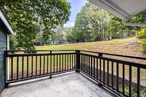 A balcony with a black railing overlooks a grassy area.