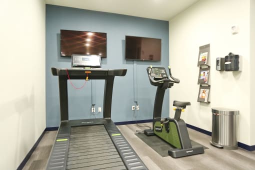 a room with a treadmill and two televisions