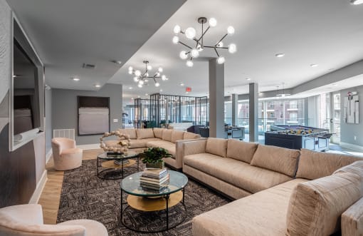 Apartments in Mt. Juliet TN - The Enclave - Common Area with Hardwood-Style Flooring, Area Rug, Sectional Couches, Armchairs, Round Glass Coffeetables, Wall-Mounted Television, Foosball and Billiards Tables, and Floor-to-Ceiling Windows
