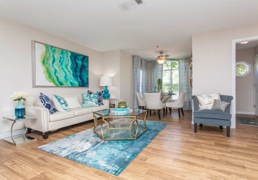 Pet-Friendly Apartments in Stockbridge, GA - Avenue 33 - Living Room with Wood-Inspired Plank Flooring, a Dining Area With a Ceiling Fan, and Windows with Blinds.