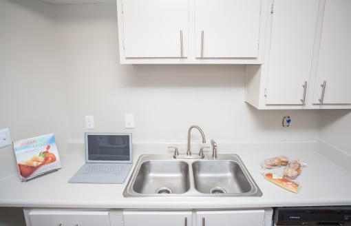 a kitchen with a sink and a laptop computer on the counter