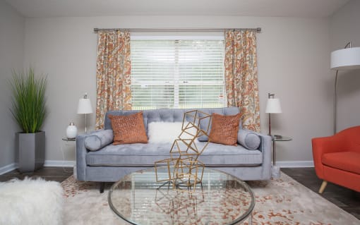 Dog-Friendly Apartments in Atlanta, GA - City Park - Living Room with Modern Wood-Style Flooring, Area Rug, Couch, Armchair, Glass-Top Coffee Table, End Tables with Lamps, Floor Lamp, and Large Window.
