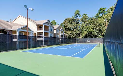A tennis court is surrounded by apartment buildings.