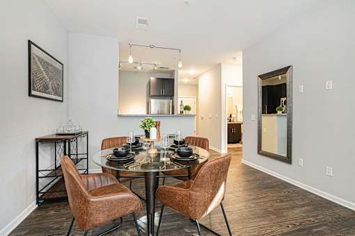 A dining room with a glass table and brown chairs.