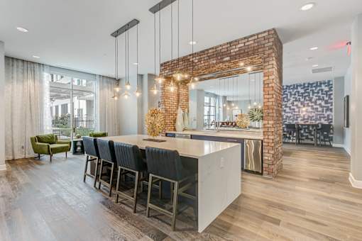 A kitchen with a brick wall and a long island with chairs.