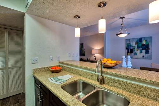 A kitchen with a sink and a bowl of fruit on the counter.