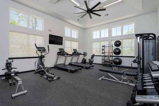 Louisville, KY, Luxury Apartments with Attached Garage - The Laurel Apartments - Fitness Center With Treadmills, Elliptical Machine, Weight Bench, Dumbbell Rack, Large Windows, And A Ceiling Fan.
