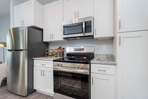 3-Bedroom Luxury Apartments In Lebanon, OH - Founders Landing - A Modern Kitchen With White Cabinetry, Salt-And-Pepper Granite Countertops, And Frigidaire Stainless Steel Appliances.