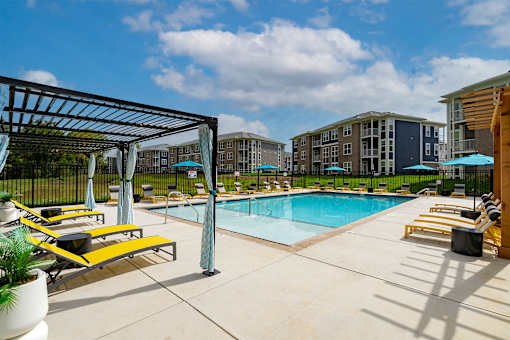 Luxury Apartments with Attached Garage in Louisville, KY - The Laurel Apartments - Swimming Pool With Lounge Chairs, Blue Umbrellas, Covered Seating, Apartment Buildings, And A Bright Sky.